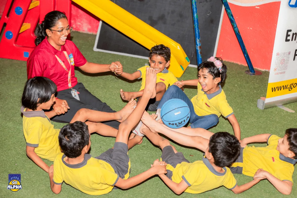 A Go Alpha coach and preschool children in a Pune class laughing during a fun group activity that builds teamwork and social skills.
