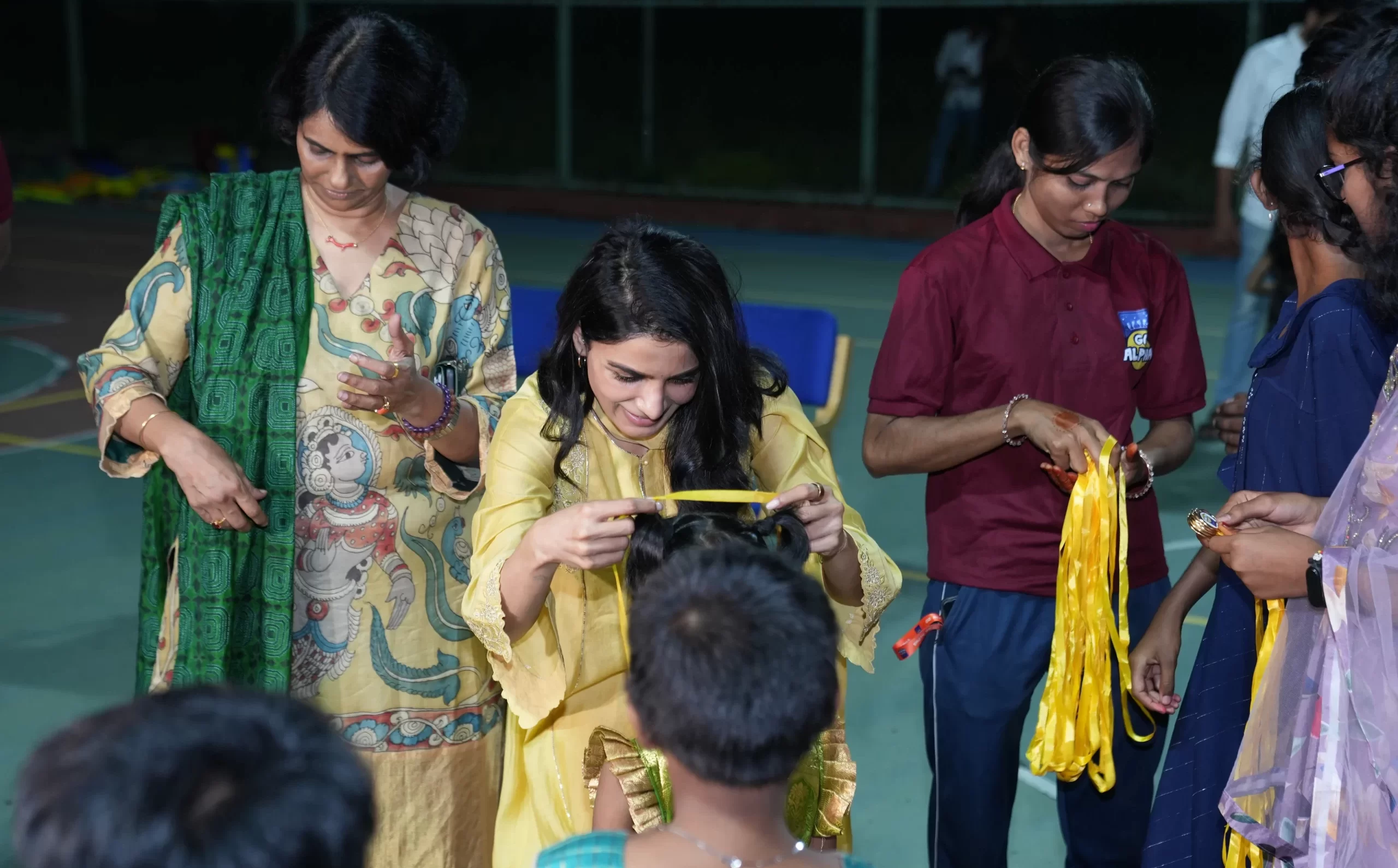 Samantha Ruth Prabhu in a yellow ethnic outfit presenting yellow medals to children at a Go Alpha outdoor sports event.
