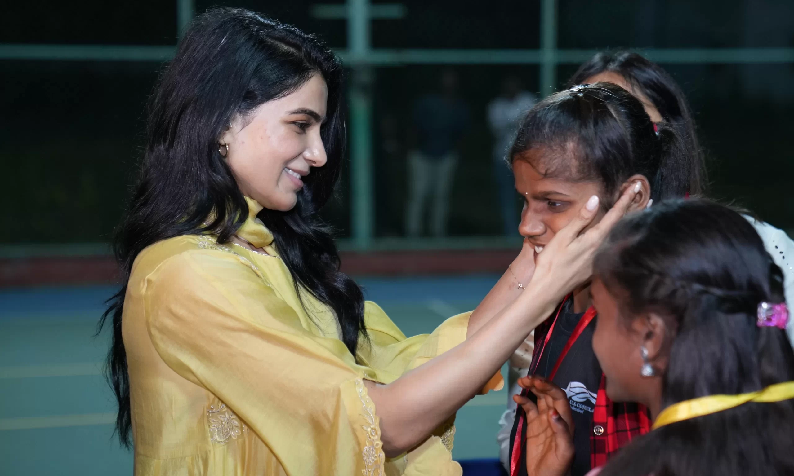 Actress Samantha Ruth Prabhu smiling with children holding lit candles during an evening community event at a Go Alpha sports venue.