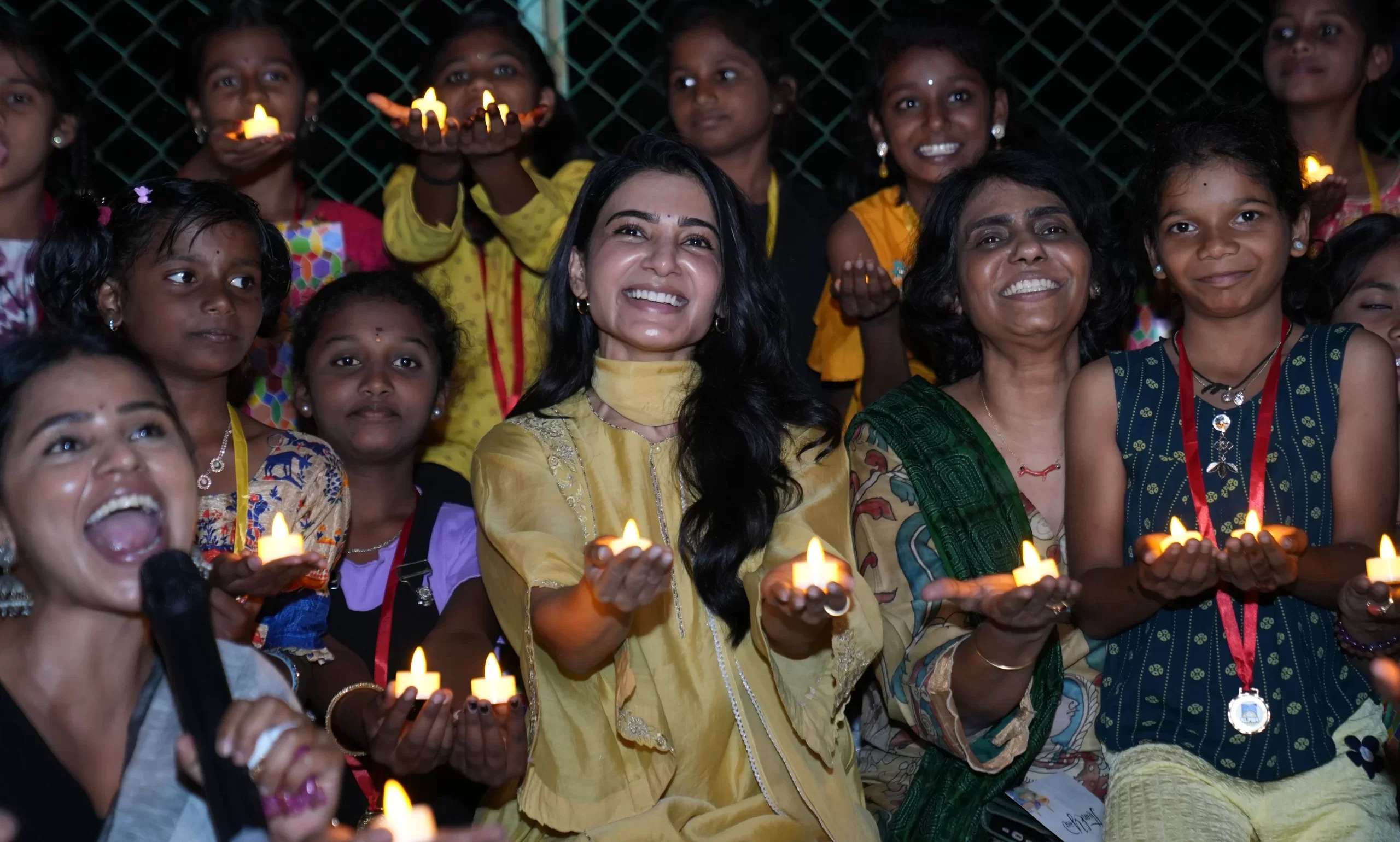 Actress Samantha Ruth Prabhu smiling with a group of young girls holding lit candles during an evening event at a sports facility